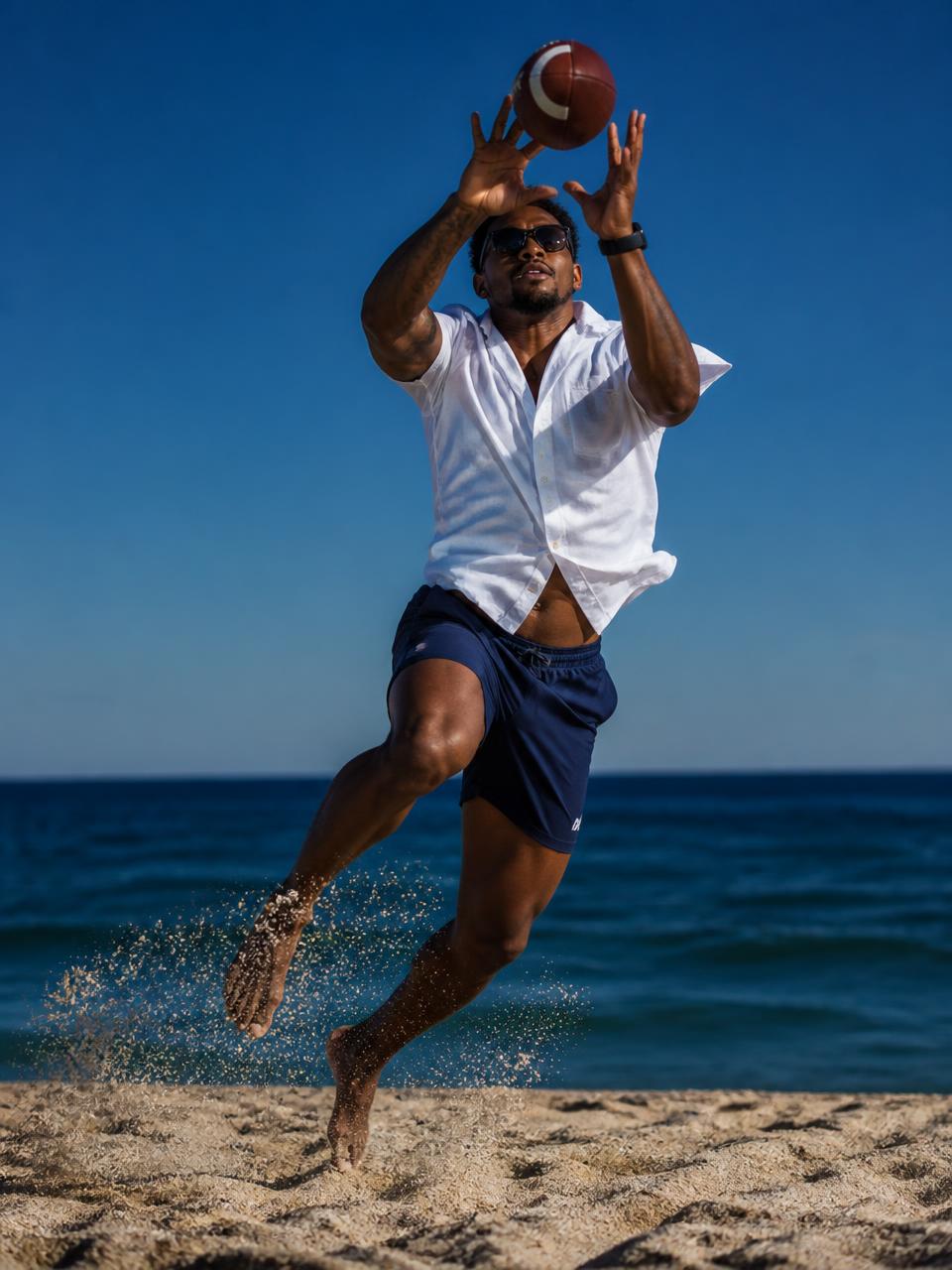 An athlete leaping mid-air to catch a football on a sunlit beach, wearing sunglasses, a white short-sleeve button-down, and blue shorts
